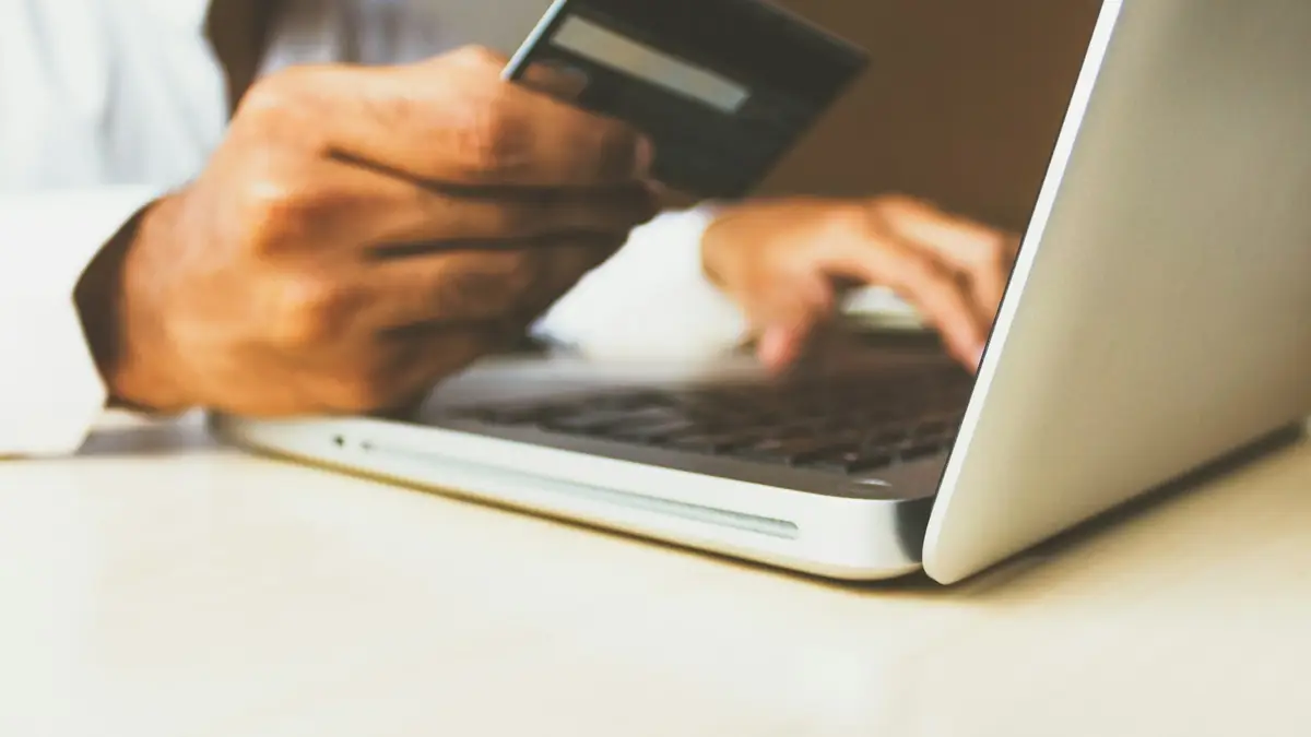 A person holding a credit card while paying on a laptop