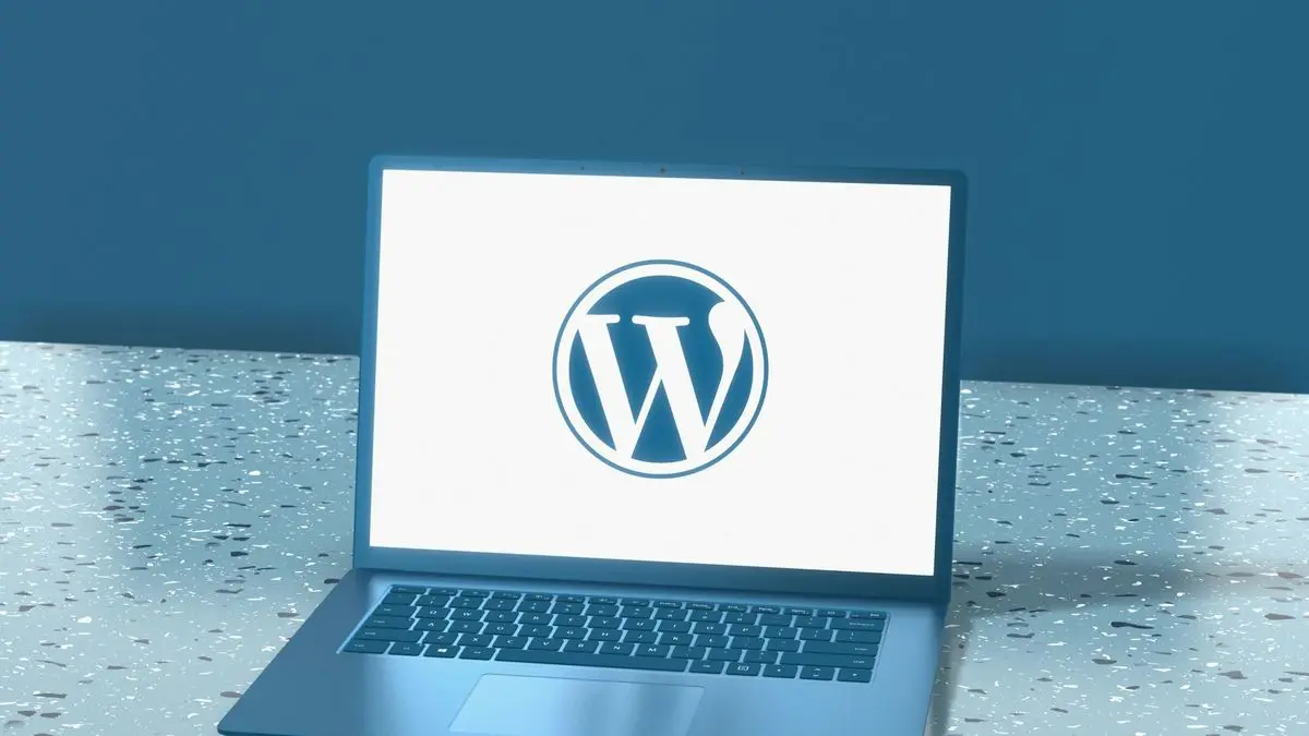 A laptop on a speckled blue surface showing the WordPress logo